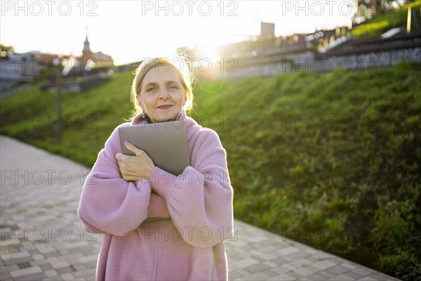 Woman embracing laptop while standing outdoors at sunrise