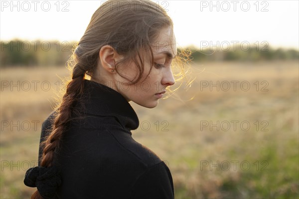 Side view of serious woman standing in field at sunset