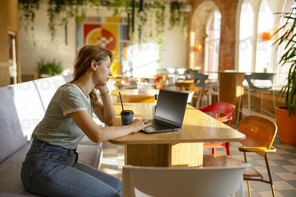 Side view of woman working on laptop while sitting in cafe