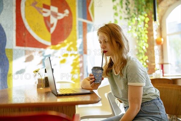 Side view of woman working on laptop while drinking coffee in cafe