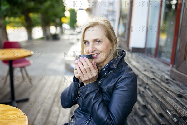 Portrait of smiling woman drinking coffee in sidewalk cafe