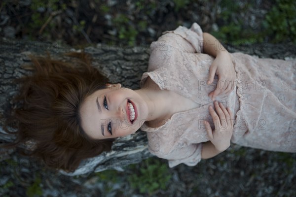 Portrait of smiling woman lying on tree trunk