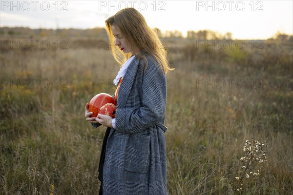 Side view of woman holding pumpkins in field