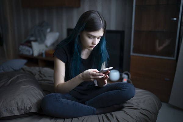 Serious woman using smart phone while sitting on bed