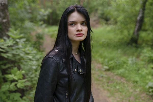 Portrait of thoughtful woman in leather jacket while standing in forest