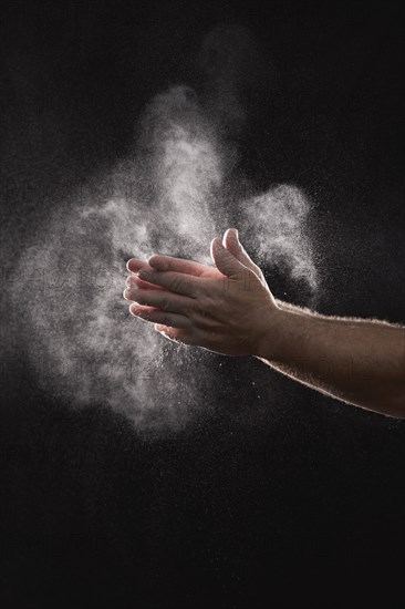 Baker dusting flour off his hands against black background