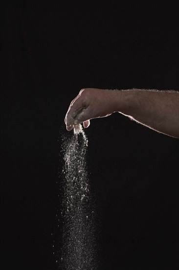 Baker sprinkling flour against black background