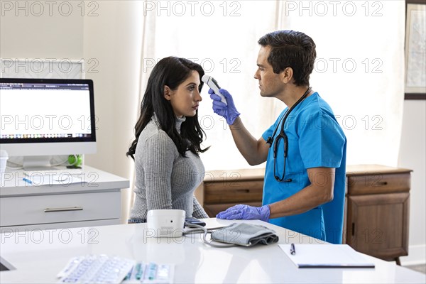 Nurse checking patients temperature in examination room