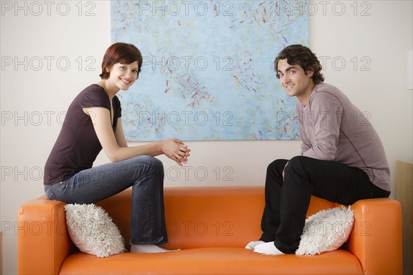 Young couple sitting on sofa and looking at camera