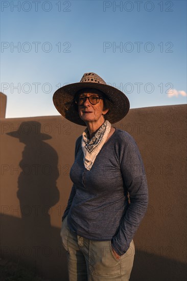 Usa, New Mexico, Santa Fe, Portrait of woman in straw hat standing against adobe wall in High Desert