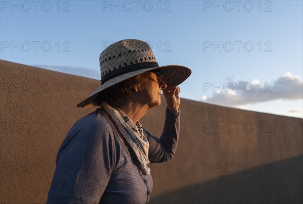 Usa, New Mexico, Santa Fe, Woman in straw hat standing against adobe wall in High Desert