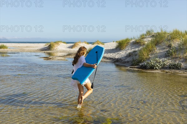 South Africa, Hermanus, Teenage girl walking on beach with body board