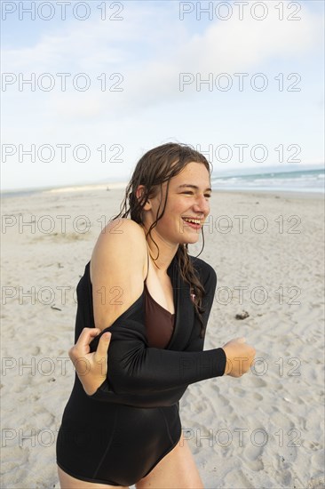 South Africa, Hermanus, Teenage girl putting on wetsuit on beach