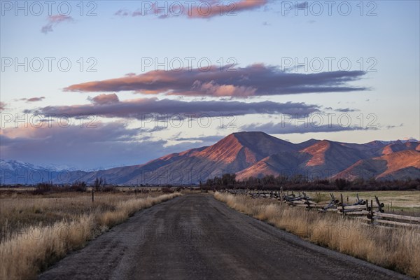 Empty dirt road leading to foothills at sunset