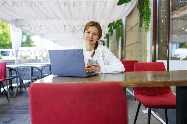 Portrait of smiling woman with smart phone and laptop at cafe table