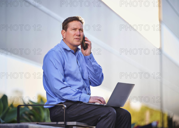 Man working on laptop and talking on phone outdoors