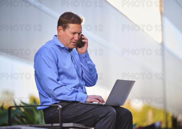 Man working on laptop and talking on phone outdoors