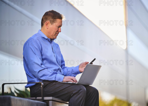 Man working on laptop and looking at phone outdoors