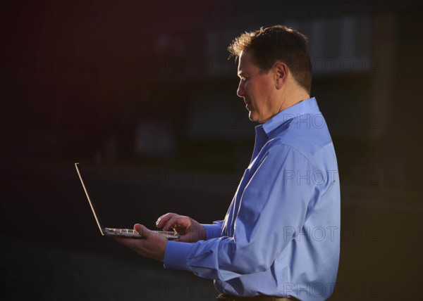 Man working on laptop and talking on phone outdoors