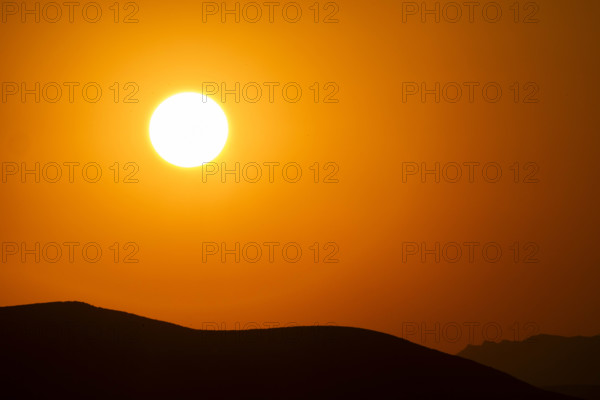 USA, Idaho, Bellevue, Setting sun over hills against orange sky