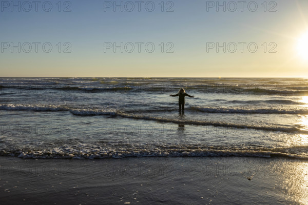 USA, Oregon, Cannon Beach, Woman wading in surf at sunset