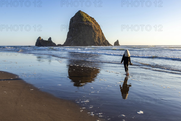 USA, Oregon, Cannon Beach, Rear view of woman walking on beach near haystack rock
