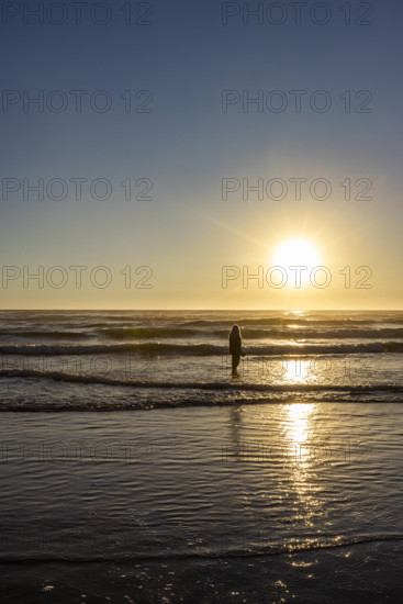 USA, Oregon, Cannon Beach, Woman standing in ocean at sunset