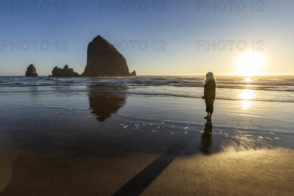 USA, Oregon, Cannon Beach, Woman standing on beach near haystack rock at sunset