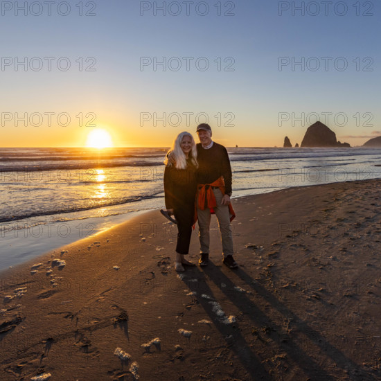 USA, Oregon, Cannon Beach, Portrait of smiling senior couple on beach with haystack rock in background