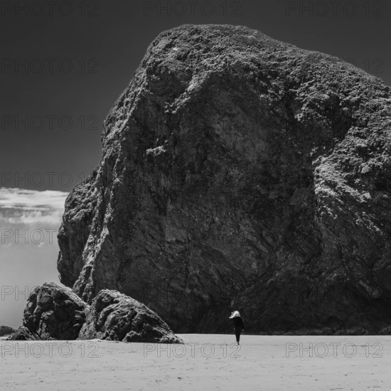 USA, Oregon, Brookings, Rear view of woman walking by huge rocks on Oregon beach, black and white