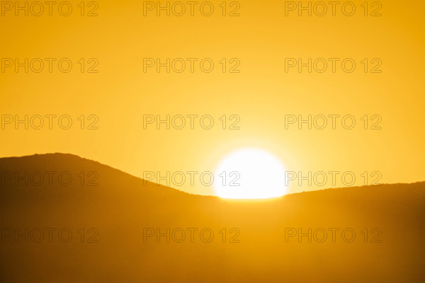 Sun setting behind hill against golden sky