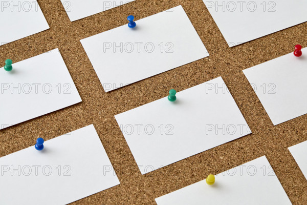 Blank pieces of paper attached to cork board with colorful push pins