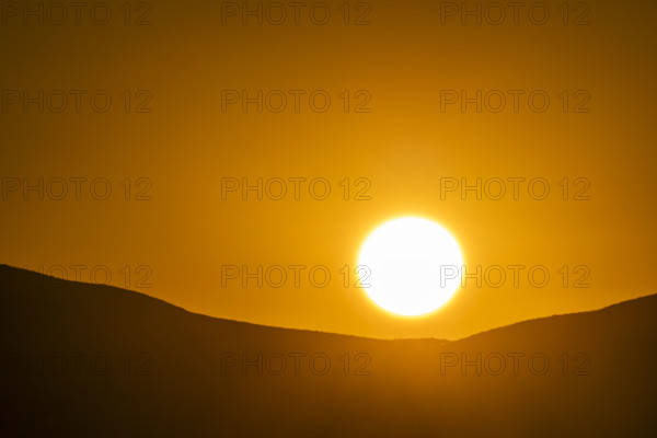 Sun setting over hills against orange sky