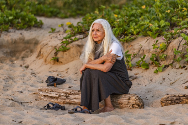 Senior woman sitting on beach at sunset