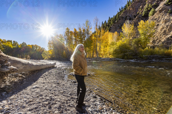 USA, Idaho, Hailey, Senior blonde woman at river in autumn