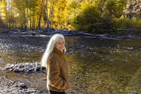 USA, Idaho, Hailey, Portrait of senior blonde woman at river in autumn