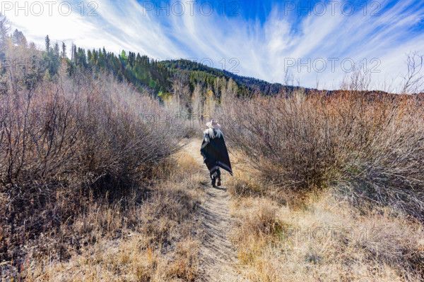 USA, Idaho, Sun Valley, Rear view of woman in wool poncho on footpath in landscape