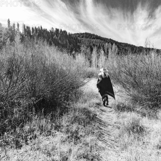 USA, Idaho, Sun Valley, Rear view of woman in wool poncho on footpath in landscape