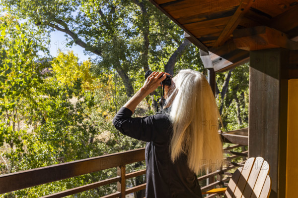 Senior blonde woman using binoculars on porch in autumn