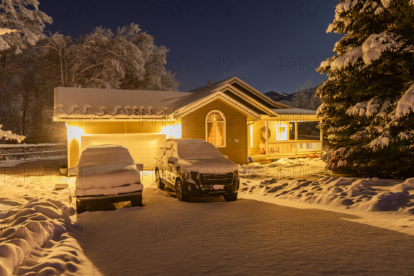 USA, Idaho, Bellevue, Illuminated suburban house and cars covered with snow at night