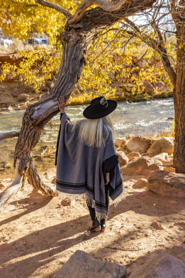 USA, Utah, Zion National Park, Rear view of woman in poncho and hat standing by tree along Virgin River