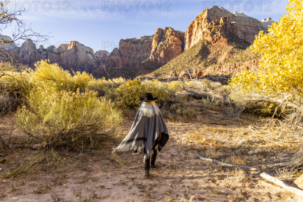 USA, Utah, Zion National Park, Rear view of woman in poncho and hat walking near Virgin River