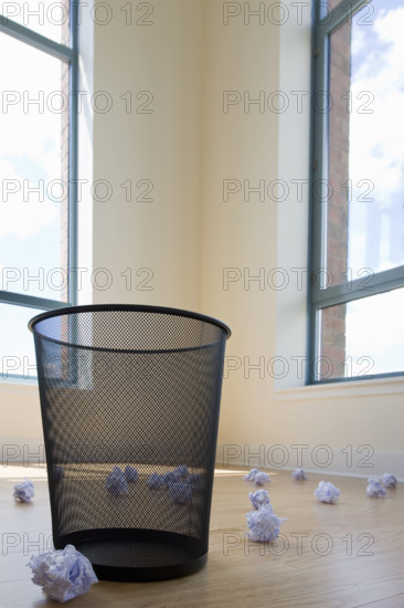 Crumpled waste paper on floor around empty bin