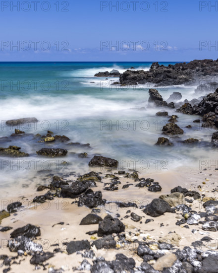 Motion blurred ocean waves washing rocks on beach. Kona, Hawaii, USA.