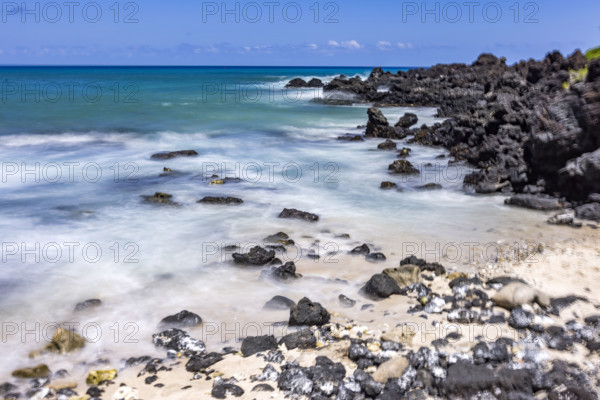 Motion blurred ocean waves washing rocks on beach. Kona, Hawaii, USA.