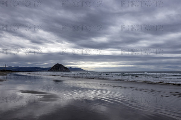 Storm clouds above beach with Morro Rock in distance, Morro Bay, California, USA.
