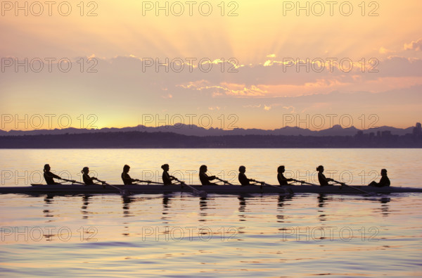 Silhouettes of team rowing boat in bay at sunset, Bainbridge Island, Washington, USA.