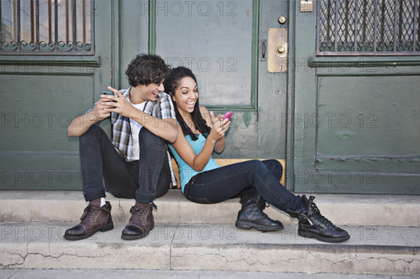 Couple using cell phones on front stoop, Los Angeles, California, USA.