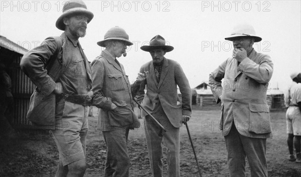 European settlers, Kenya. Exterior shot of four mature European men engrossed in conversation. All of the men wear hats: two carry walking sticks. Kenya, circa 1935. Kenya, Eastern Africa, Africa.