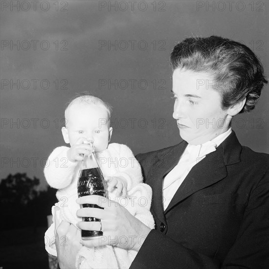 Coca Cola baby. Wendy Winter holds a bottle of Coca Cola up in front of her baby. Kenya, 22 August 1954. Kenya, Eastern Africa, Africa.